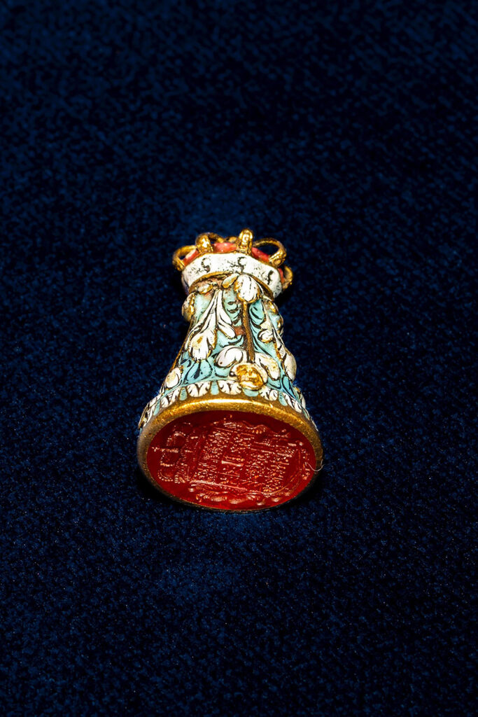 Een rode lakstempel met een wapen ligt op zijn zij. De bovenkant heeft veel kleuren en een kroon op de top.