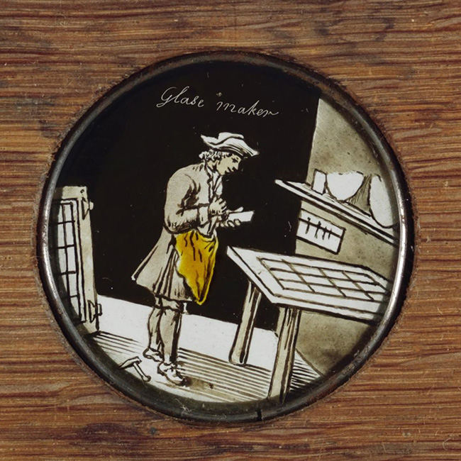 'glase maker', met een ruitje in zijn hand, voor hem een groot raam plat liggend op een tafel.