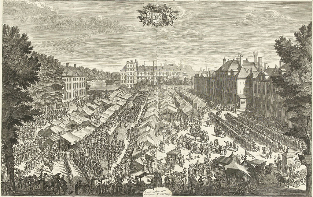 Een prent met een vogelvluchtoverzicht van de kermis in Den Haag met op de achtergrond het binnenhof. Op het plein staan allemaal tentjes opgesteld met een paar brede ruimtes ertussen. Daar paradeert de schutterij. Rechts staat de cavalerie en overal zijn mensen wat aan het doen, onderweg. HEt is echt een kijkplaat.