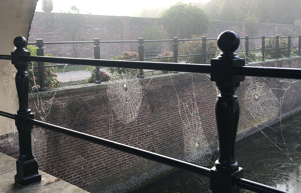 Foto vanaf de onderbrug van Kasteel Amerongen richting de kade. In de balustrades van de onderbrug hangen spinnenwebben.