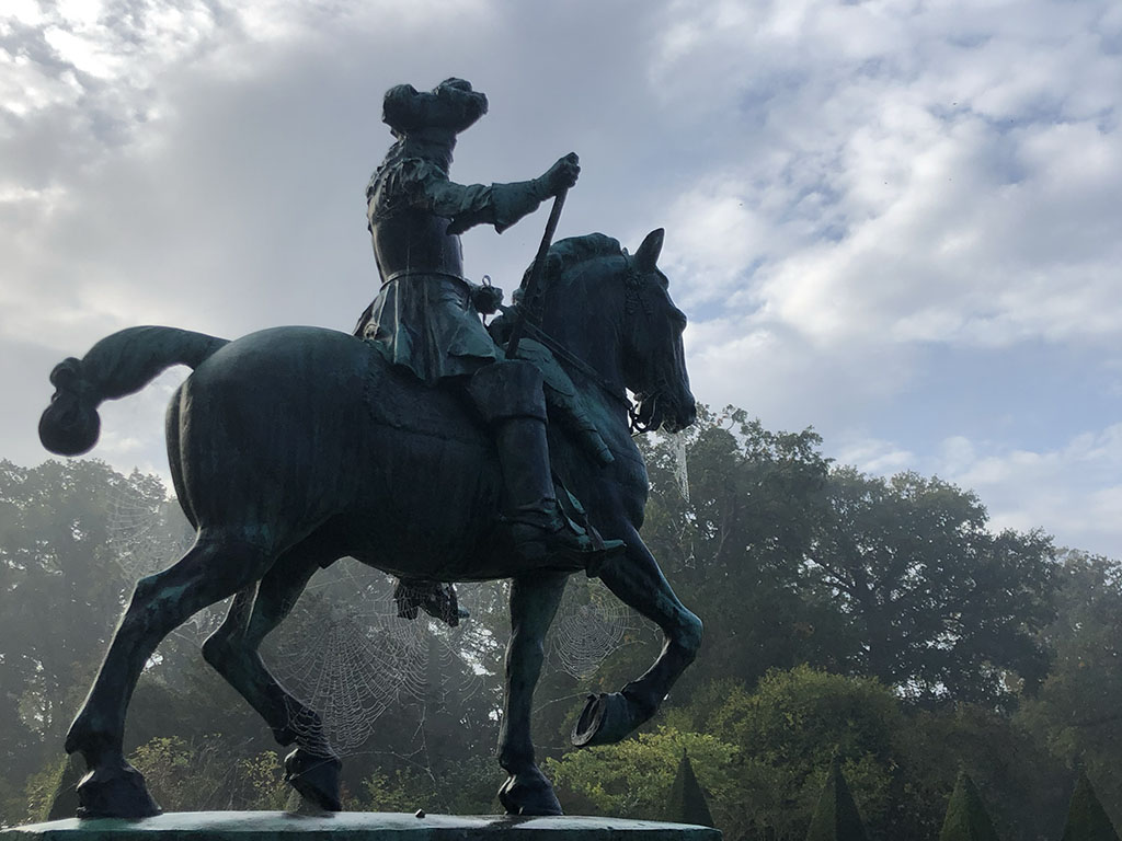 Tegen een dreigende lucht en een bomenrijke achtergrond staat het standbeeld van Willem III te paard. We zien het standbeeld van rechtsonder, het paard stapt naar rechts, Willem III heeft in zijn linkerhand de teugels en in zijn rechterhand een maarschalkstaf. De staat van het paard is opgeknoopt. Tussen het buik en de benen en tussen de neus en de benen zitten spinnenwebben met dauw erop.