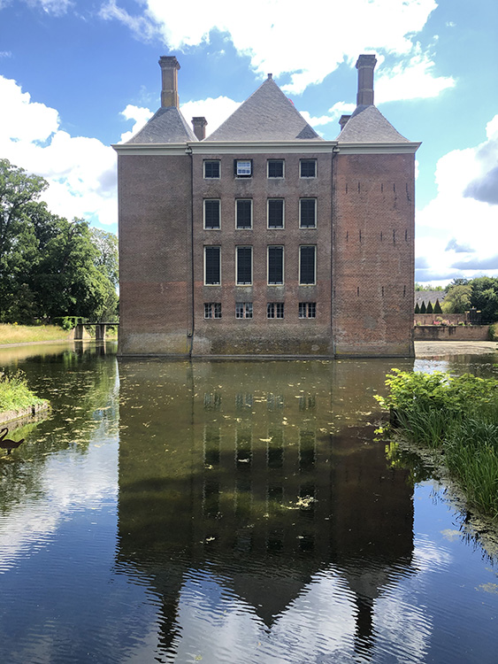 Van achter lijkt het huis twee torens en een middendeel te hebben. Elk deel heeft een eigen puntdak. Het middelste dak is het breedst en het hoogst. Op de twee puntdaken aan de zijkant zitten schoorstenen. In het middendeel zitten vier ramen naast elkaar, onder de kleinere ramen van de kelder, daarboven elke verdieping kleinere ramen. De rechter 'toren' heeft een duidelijk andere kleur en in de muur zijn trekken (metalen banden) verwerkt. Het kasteel ligt in een gracht en weerspiegelt in het water. Aan deze kant zit geen ingang of brug.