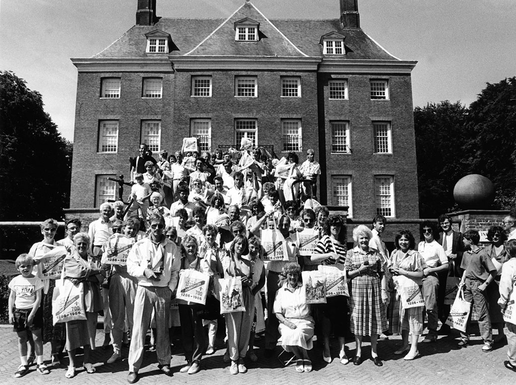 Een zwartwit bordesfoto van een uitbundige groep in zomerse kleding die tassen laten zien met 700 Amerongen.