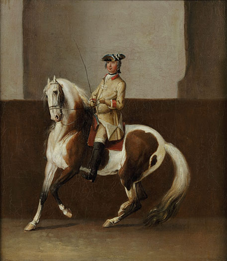 Een man in een beige pak zit op een gevlekt paard. Het paard gaat naar links, lijkt vaart te maken en naar links af te buigen. Het paard heeft witte manen en een witte staart die aan de onderkant vuilig is.