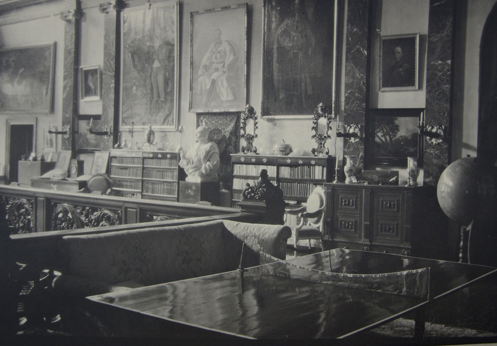 Zwartwitfoto van de galerij. Veel elementen van de huidige galerij zijn herkenbaar: de portretten, de buste van de keizer, op bijna alle kastjes en kisten staan vazen, schalen, spiegels, glas en andere objecten. De Kandelaars met handen uit de muur hebben nog echte kaarsen. Links de balustrade met het houtsnijwerk van Joseph Cuypers, daarvoor staat een bank en daarvoor een tafeltennistafel.