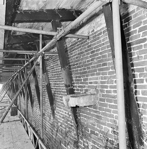 Zwartwitfoto van een draagconstructie tegen een stenen muur.