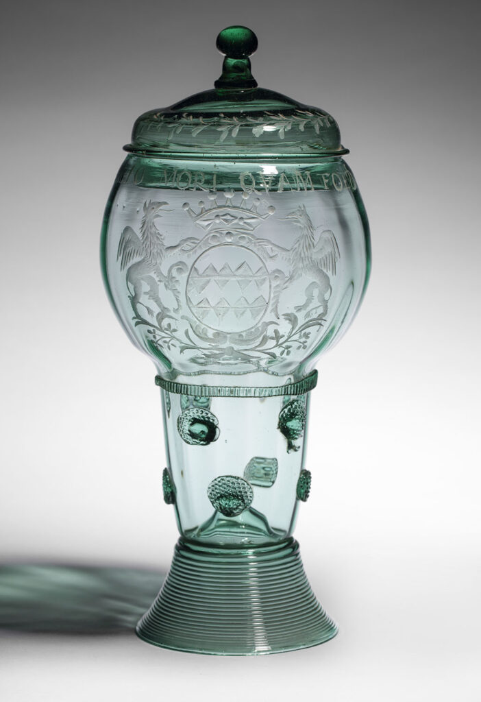 Roemer met deksel van donkergroen glas. Hoog gesponnen voetje. Van boven open stam, bezet met twee rijen platte braamnoppen, gestempeld in een fijn patroontje. Bolle cuppa, van de stam gescheiden door een geknepen draad. Met het rad gegraveerd het gekroonde wapen van Reede, opgehouden door twee griffioenen. Erboven het devies: "Malo mori Quam Foedari". Licht gewelfde deksel met een bol knopje, langs de rand een takmotief.