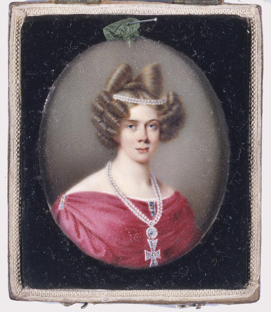 Portretminiatuur in de vorm van een borststuk van prinses Marianne, en face naar rechts weergegeven. Zij draagt een cyclaamrode jurk met lage ballonmouwen, meerkleurige decoratie op de schouders en het lijfje en een dubbele ketting van parels met een diamanten kruis. Het haar is gekruld en versierd met een dubbele parelketting en een strik van nephaar. De prinses is voor een groenbruin gestippelde achtergrond geplaatst.