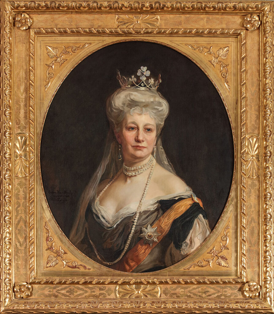 Ovaal busteportret van Keizerin Auguste Victoria tegen een donkere achtergrond in een zware vergulde lijst. De keizerin zit met haar lichaam naar links en kijkt weg naar rechts. Ze heeft haar haar hoog opgestoken met daarin een klaverbladdiadeem, waaraan een lange, witte sluier is bevestigd. Ze draagt een lange parelketting en lange oorbellen. Haar jurk heeft een diep decolleté en laat de schouders bloot. Ze draagt een oranje sjerp met daarop de borstster van de Orde van de Zwarte Adelaar.