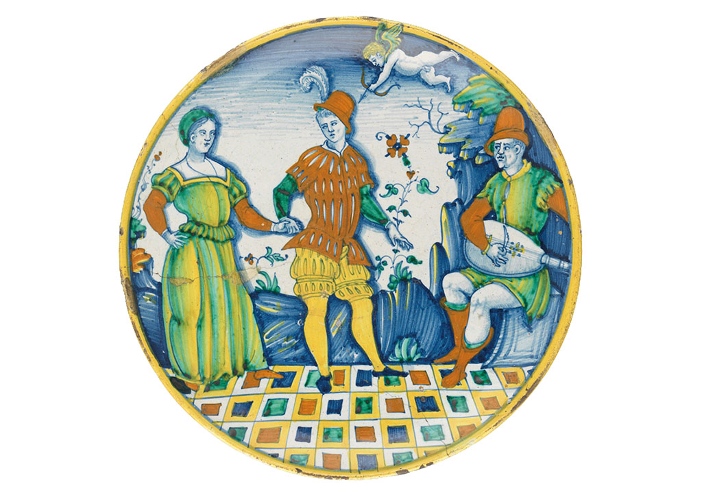 Bord beschilderd met blauw, geel, groen en rood. Op een tegelvloer met bonte kleuren staat een stel, zij met een groengele jurk, hij met een rood jak en een gele broek. Boven hen vliegt cupido die een pijl afschiet. Rechts zit een man met een luit. Op de achtergrond een berglandschap met bloemen.