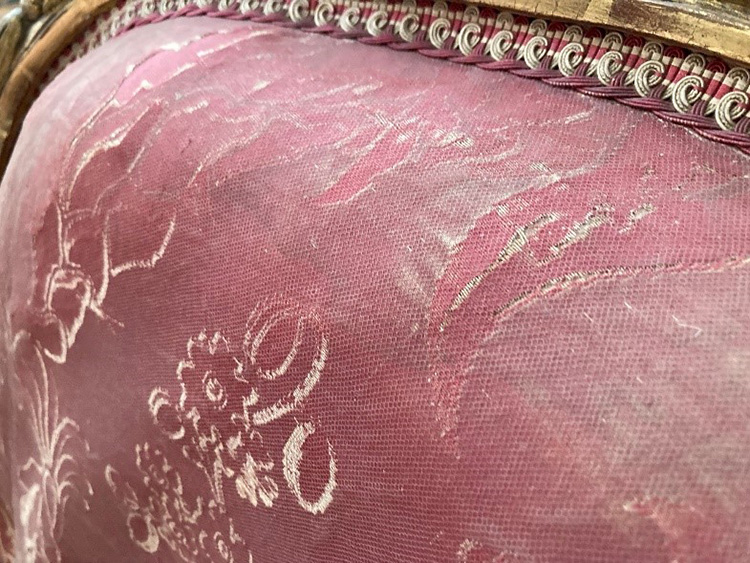 Bovenkantvan een rugleuning van een stoel. In de bekleding zie je heel duidelijk waar de stof vastgenaaid of zelfs vervangen is. Over de stof heen zie je het netmotief van tule.