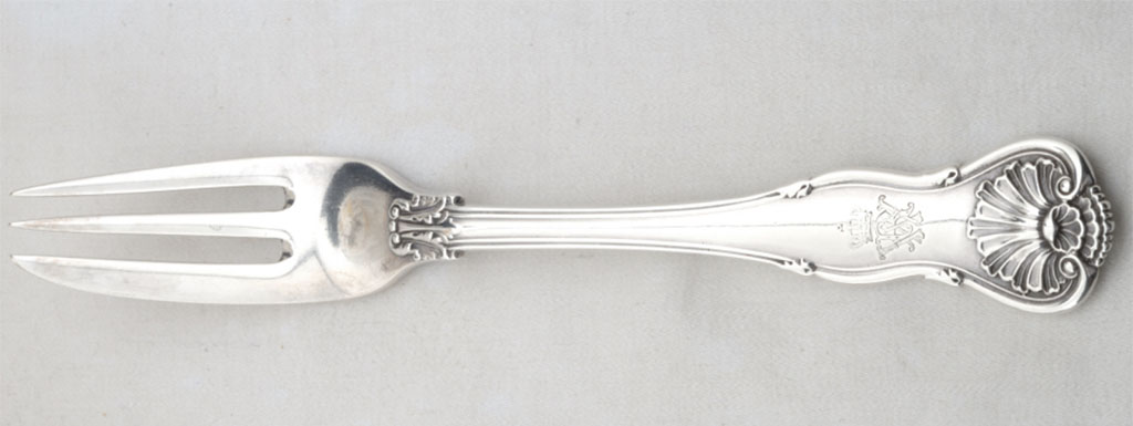Een zilveren vork met gelobd vioolvormige steeluiteinde met smaller toelopende steel. Drietandige vork, de linker tand dient ook als snijmes. Uiteinde steel is gedecoreerd met schelpmotief en daaronder zit een gekroond WR monogram.