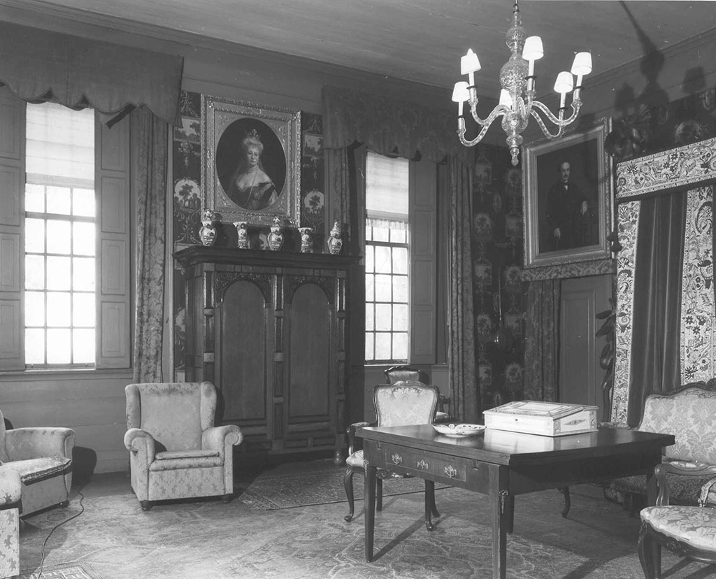 Zwartwit foto van de zuidkant van de koningskamer. Tussen de ramen staat een massieve kast met daarop een vijfdelig kaststel. Daarboven hangt een portret van keizerin Auguste Victoria in een zware lijst. In de westmuur aan de rechterkant zit een door met daarvoor een gordijn. Boven de deur hangt een portret van Jules Auguste van Bylandt. Aan het plafond hangt een eenvoudige glazen kroonluchter, rechts zien we nog net een deel van het hemelbed. Op de voorgrond een tafel met daarop een bord en een ivoren schrijfdoos. Eromheen een paar fauteuils. Links staan wat moderne leunstoelen.