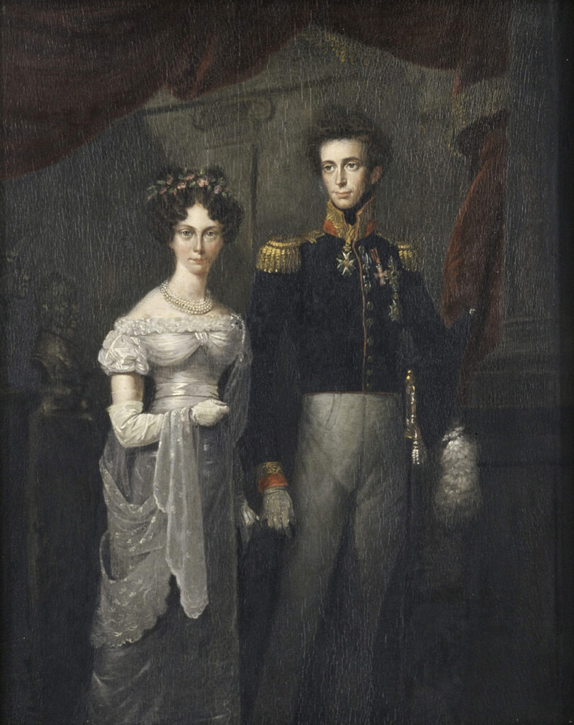 Een portret van een man en een vrouw. De vrouw draagt een elegante witte jurk die wat afhangt van haar schouders. Over haar gehandschoende rechterarm draagt ze een kanten sleep. Ze heeft opgestoken donkere krullen en er zitten bloemen in haar haar. Naast haar staat een donkere man met een lang, smal gezicht. Hij draagt een kort militair jasje met een hoge rode kraag en grote gouden epauletten. Op zijn linkerborst draagt hij diverse onderscheidingen. Hij draagt een lichtgrijze broek.