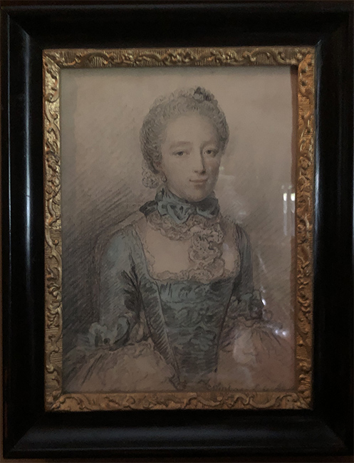 Portret van een jonge vrouw met een blauwe jurk aan met een strak lijfje. Om haar hals een witte kraag met een blauwe strik. Het portret zit in een zwarte lijst met aan de binnenkant een gouden bewerkte rand.