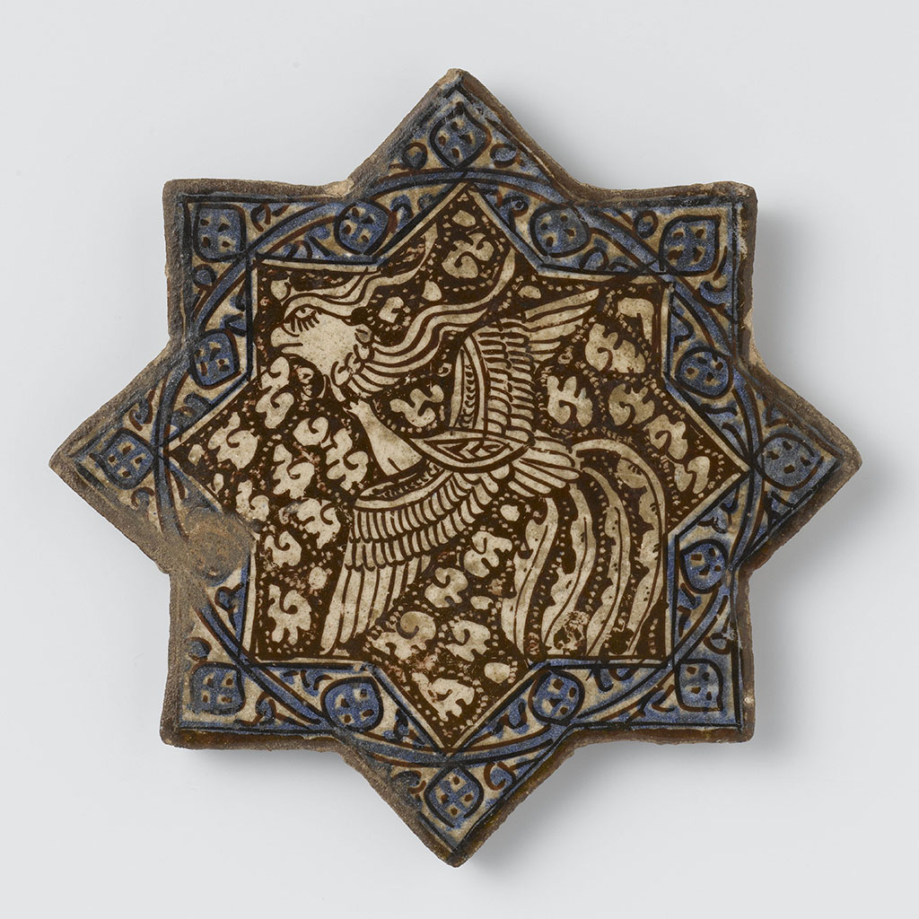 Stervormige tegel van kwarts-fritgoed met acht punten, gedecoreerd met een feniks en gestileerde bloemtak in luster en blauw op ondergrond van witte glazuur.