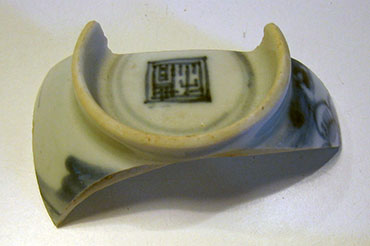 Een scherf van de onderkant van een wit kommetje met met een blauw vierkant met Chinese tekens.