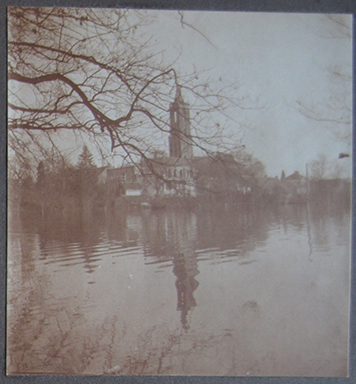 Zicht naar het dorp van het kasteel: een watervlakte met aan het eind de huizen en de kerk.