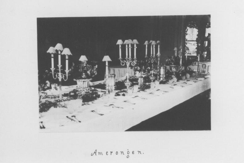 Een tafel met met bestek gedekt, op tafel staan allerlei sierstukken en kandelaars met op elke kaars een lampenkapje. 