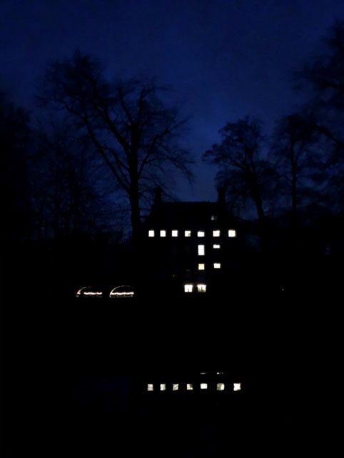 Tegen een heel erg donkere lucht een zwart kasteel Amerongen met zwarte bomen. Op verschillende plekken in huis branden nog lichtjes en sommige van die lichtjes weerspiegelen in de gracht. 