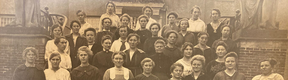 Groepsfoto van serieus kijkende dames, netjes maar eenvoudige gekleed.
