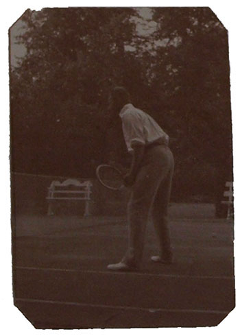 Een donkere foto van iemand die klaar staat om een bal te ontvangen. In zijn hand een tennisracket