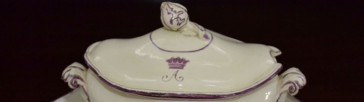 De deksel van een dekschaal met een scheve knop en een paarse A met een kroon erboven