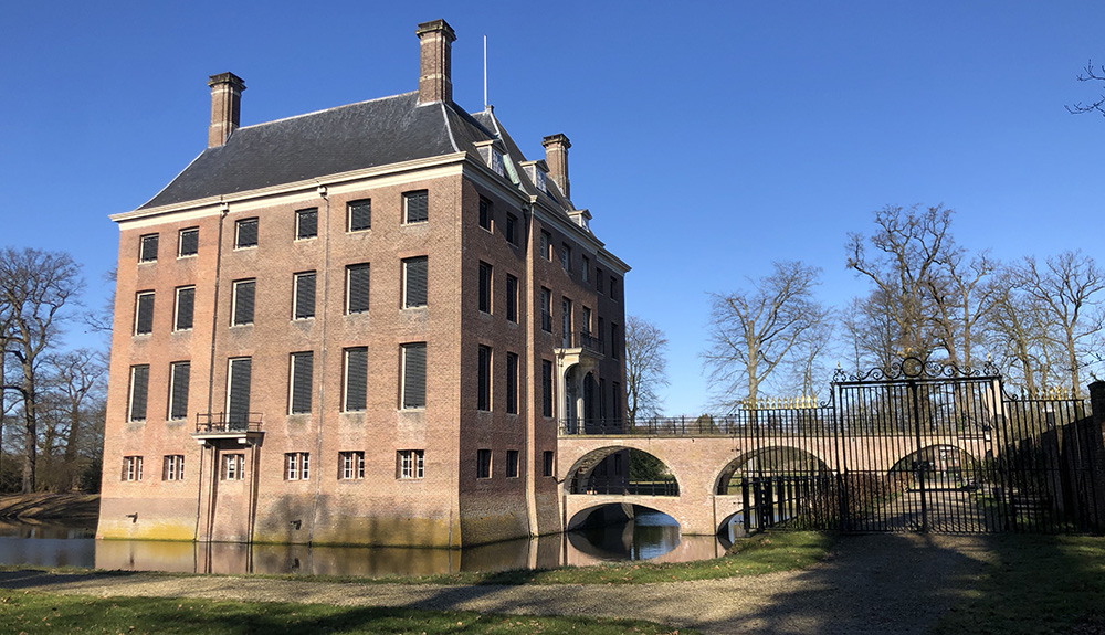 Het huis Amerongen, een bakstenen kolos met rechts de dubbele brug. Het huis heeft een breedte van zes ramen en een strak dak. 