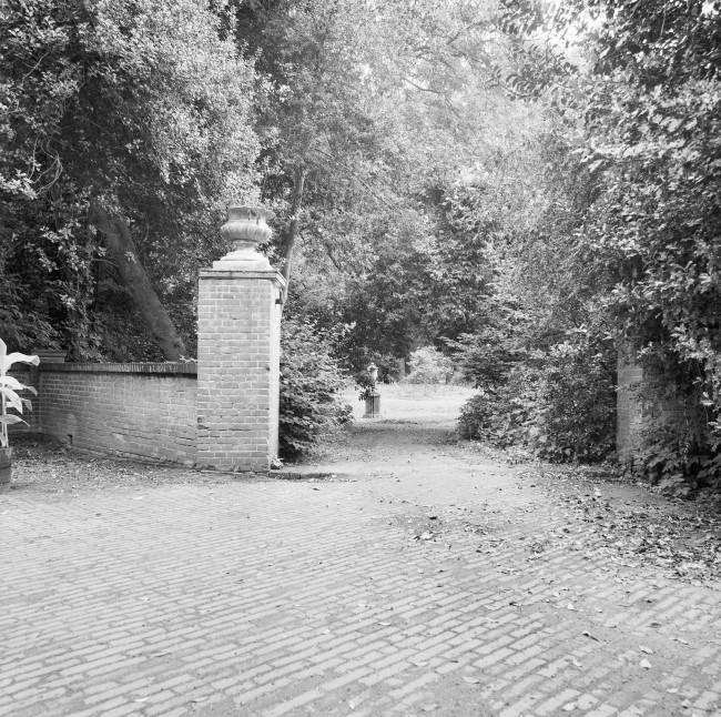 Foto van een bestraatte open ruimte met een doorgang naar de tuin. 