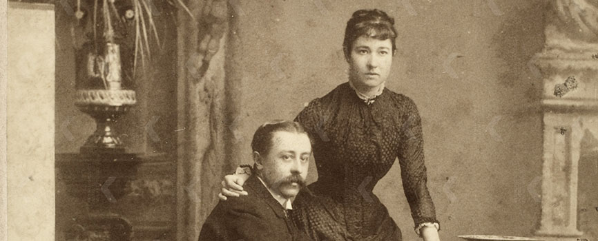 Zwartwit foto van een zittende man naast een staande vrouw die haar arm om zijn nek heeft liggen