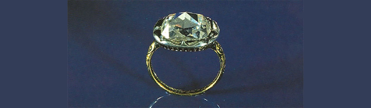 Een gouden ring met een grote diamant tegen een blauwe achtergrond.