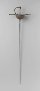 Rapier met ijzeren gevest. Ronde knop met negen ruiten. Balustervormige voorbeugel met twee zijbeugels welke gesmeed zijn aan de halve korf. Pareerstang met ballustervormige knoppen. Aan de andere zijde van de pareertstang zijn twee zijbeugels aan de korf aangebracht. Puntvormige ricasso. Rechte tweesnijdende pareerstang met aan beide zijden een geul, waarin gegraveerd aan beide zijden: xx I Z xx SOLINGEN [?] xx.