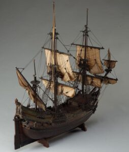 Afbeelding van een modelschip met twee grote masten, zeilen en tuigage.