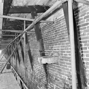 Zwartwitfoto van een draagconstructie tegen een stenen muur.