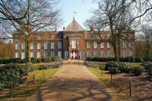 Groot symmetrisch gebouw van twee verdiepingen. In het midden een soort toren met een poort met witte deuren met een rode zandloper, daarboven en aan weerszijde een raam. Aan weerszijde vijf ramen en aan de uiteinden weer een soort soort toren met drie verdiepingen en twee ramen breed.